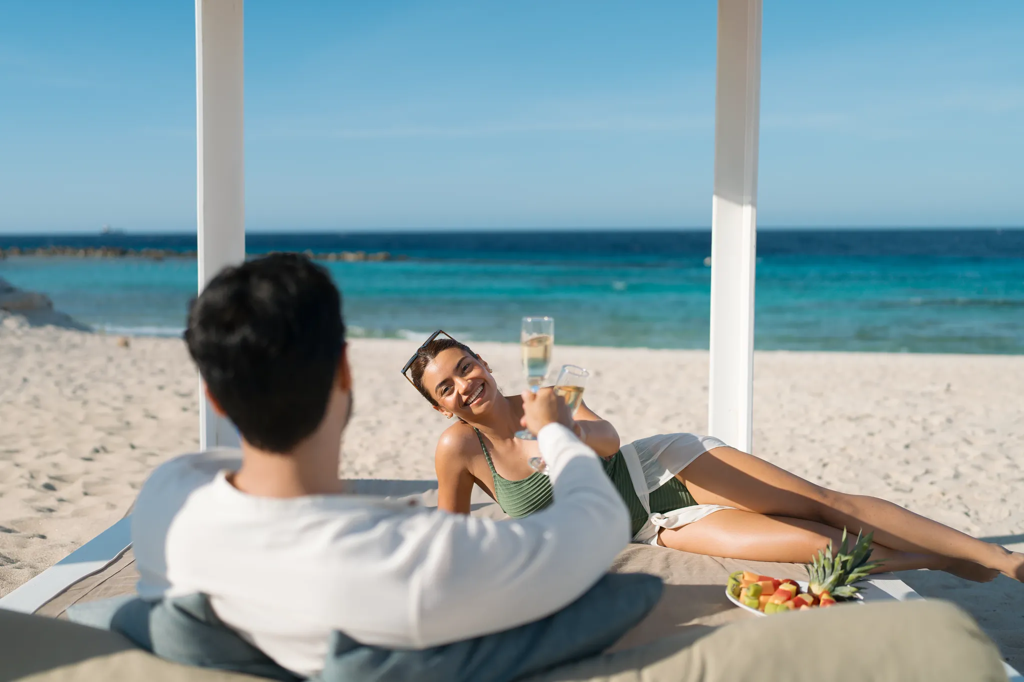 Couple toasting champagne in a beach cabana with ocean views at Dreams Curaçao Resort.