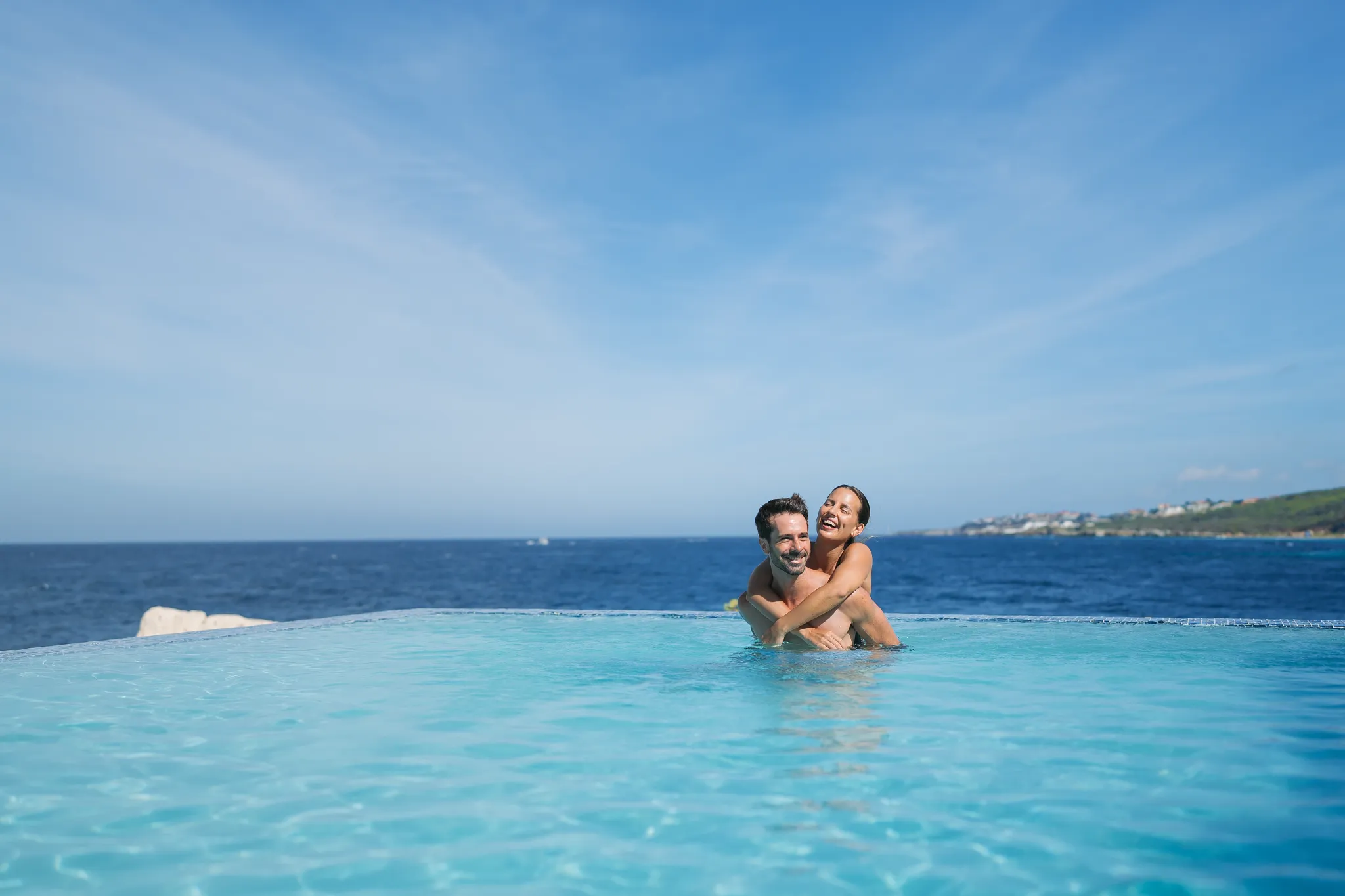 Couple embracing in an infinity pool overlooking the ocean at Dreams Curaçao Resort.