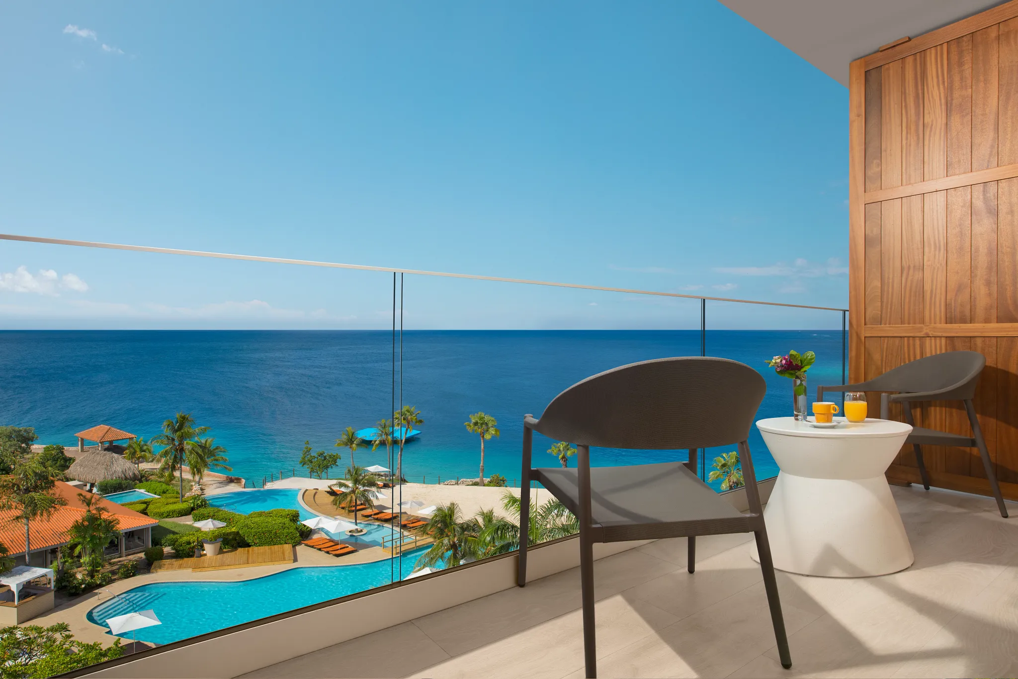 Private balcony with seating and pool view at Deluxe Pool View room in Dreams Curaçao Resort overlooking the ocean.
