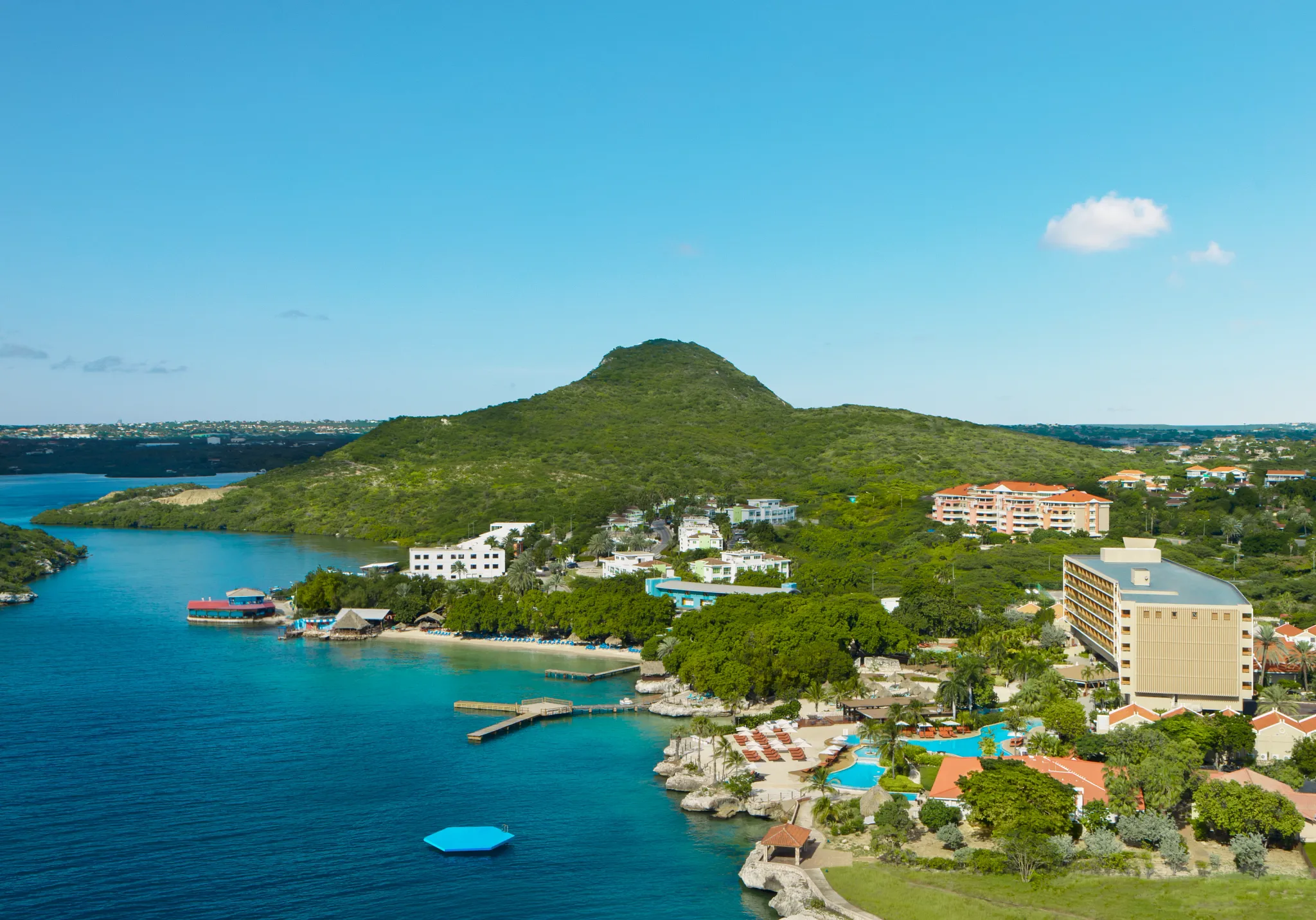 Aerial view of Dreams Curaçao Resort, Spa & Casino showcasing turquoise lagoon waters, private beach areas, and lush island landscape.