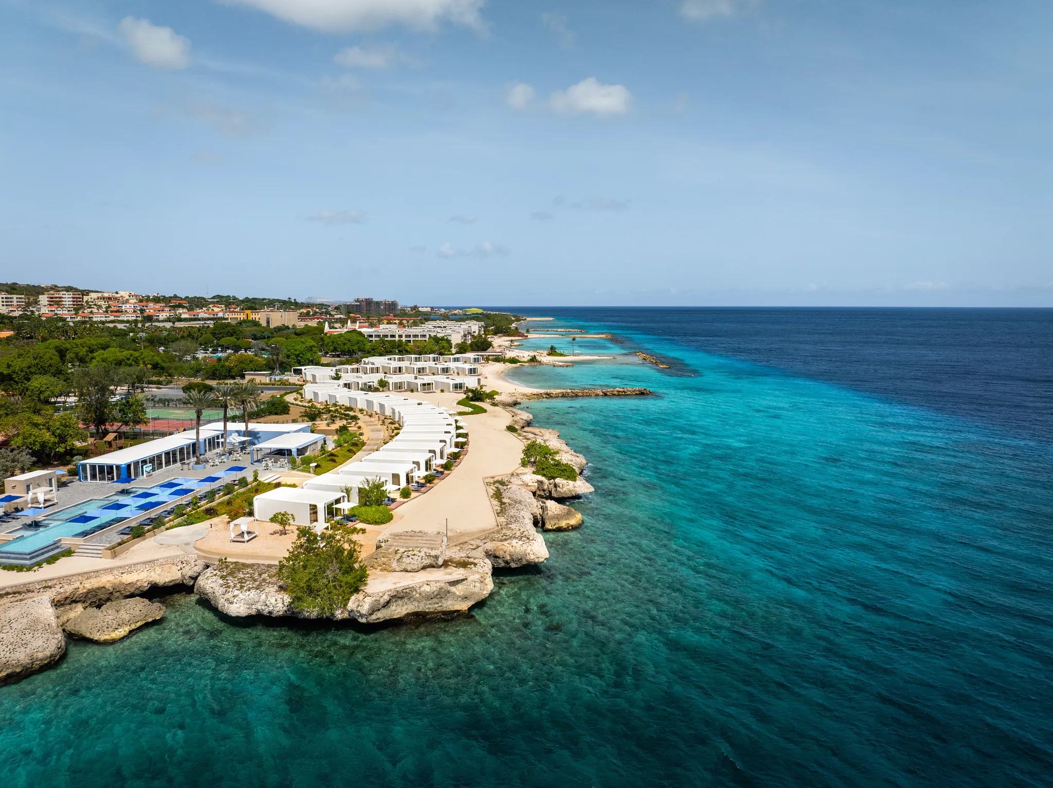 Luxury beachfront bungalows lined along the coast at Dreams Curaçao Resort with clear turquoise water views.
