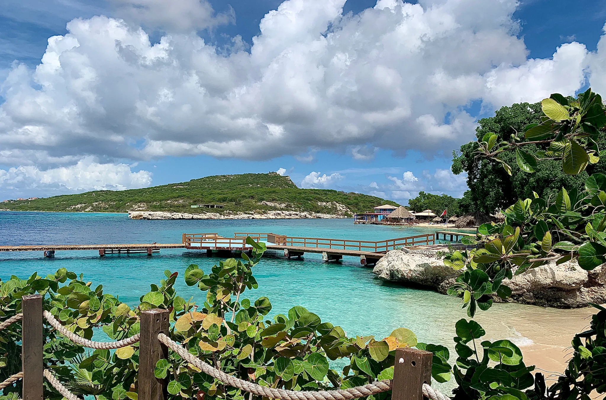 Wooden pier extending into clear blue water at Dreams Curaçao Resort with a secluded beach cove and tropical surroundings.