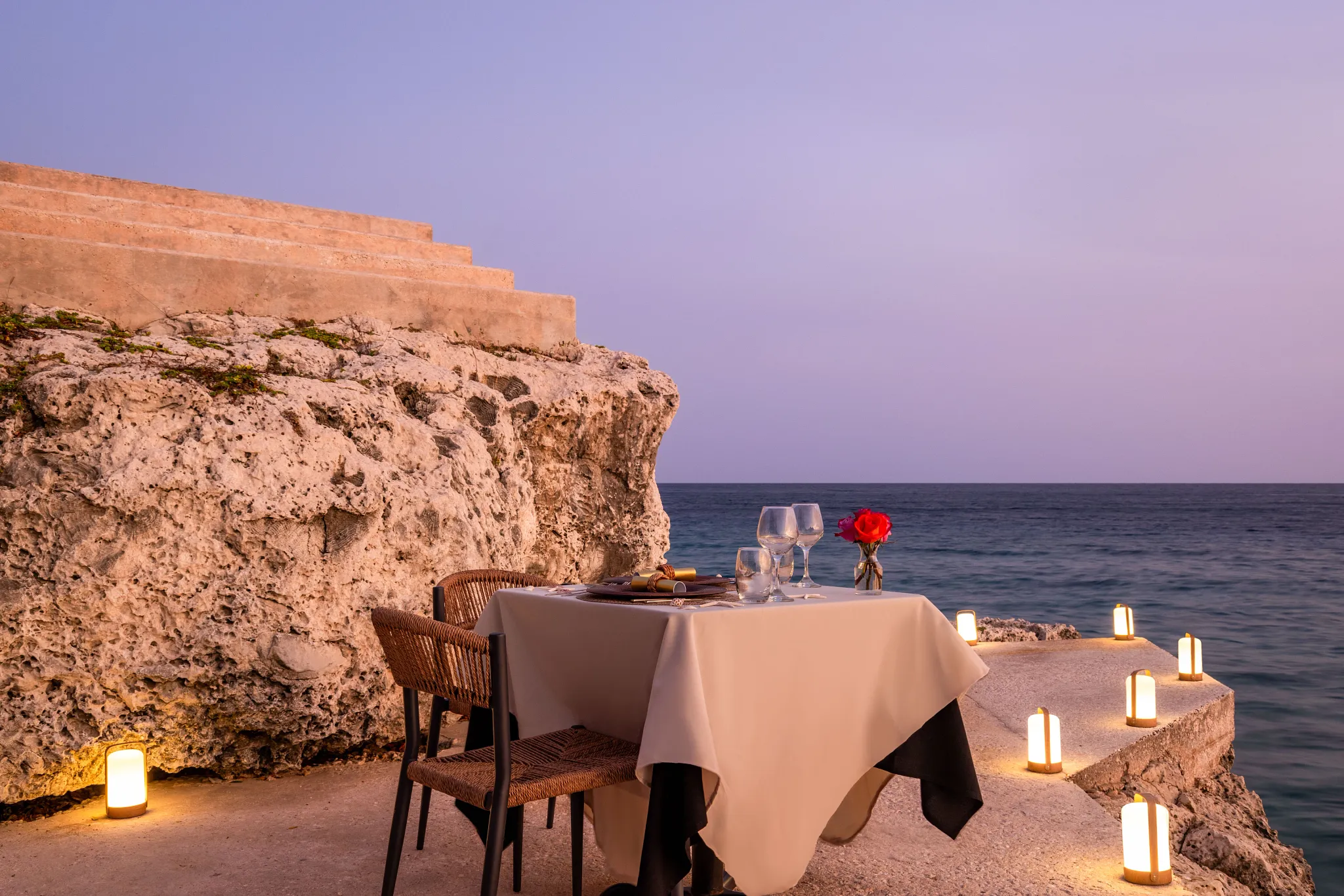 Romantic private dinner setup on a cliff overlooking the ocean at sunset at Dreams Curaçao Resort.