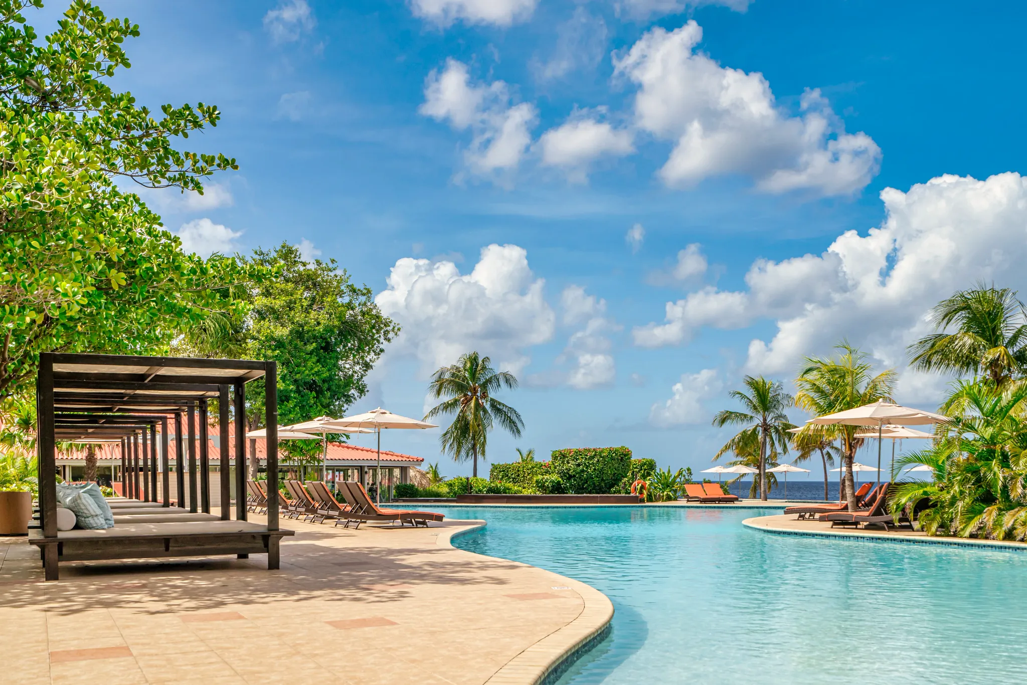 Infinity pool with cabanas and shaded loungers at Dreams Curaçao Resort overlooking the ocean.