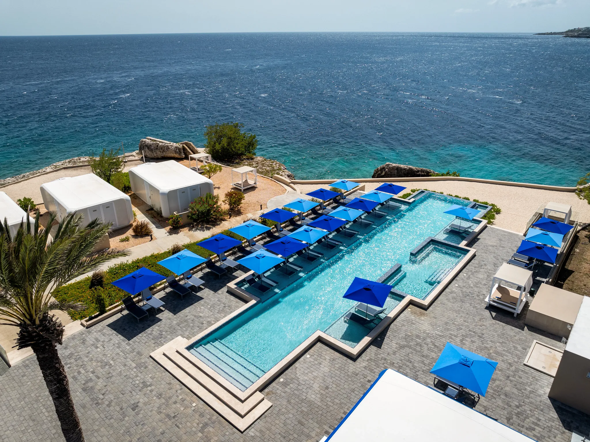 Infinity pool with blue umbrellas overlooking the Caribbean Sea at Dreams Curaçao Resort.