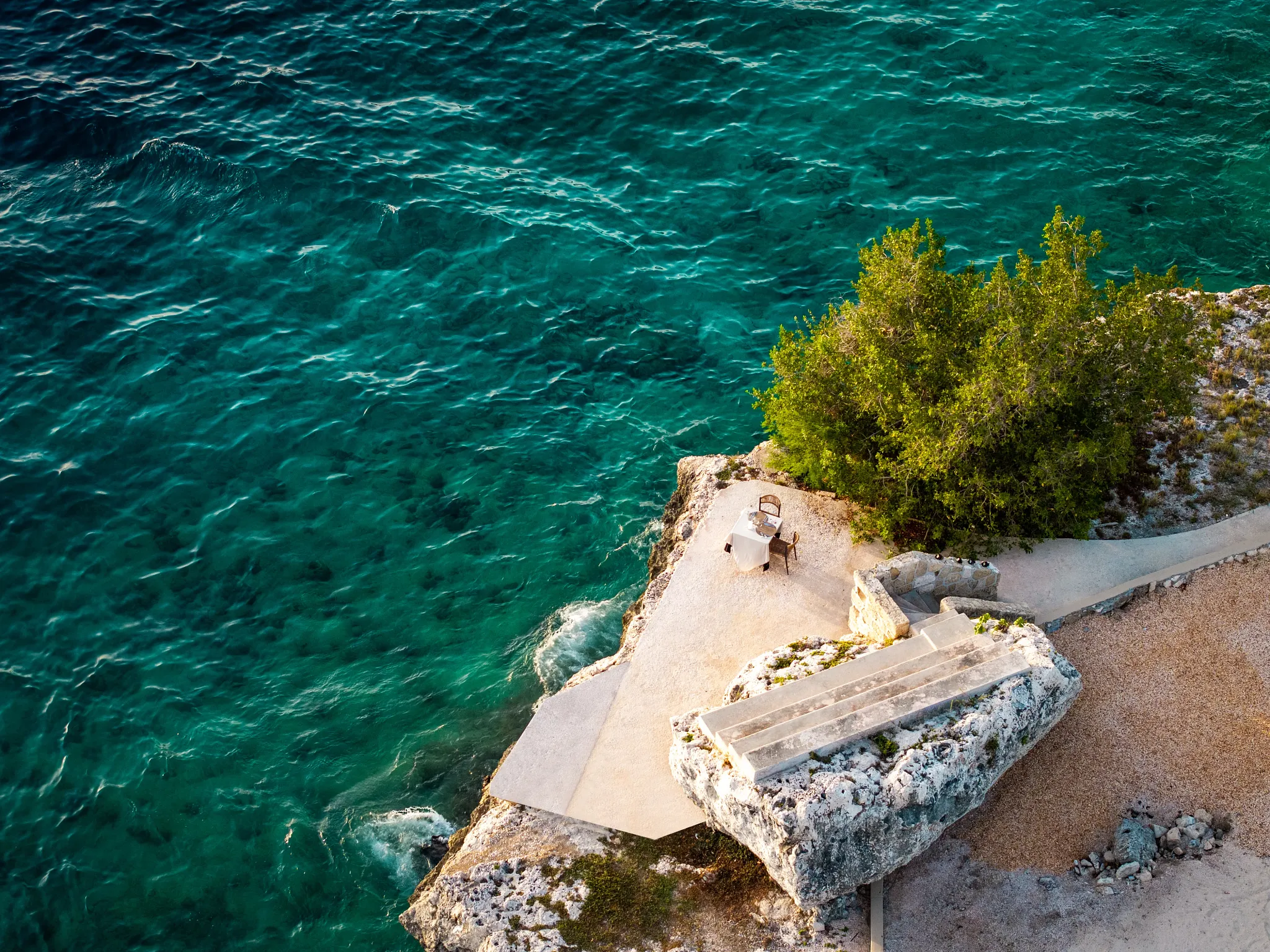 Aerial view of secluded cliffside dining setup above turquoise Caribbean waters at Dreams Curaçao Resort.