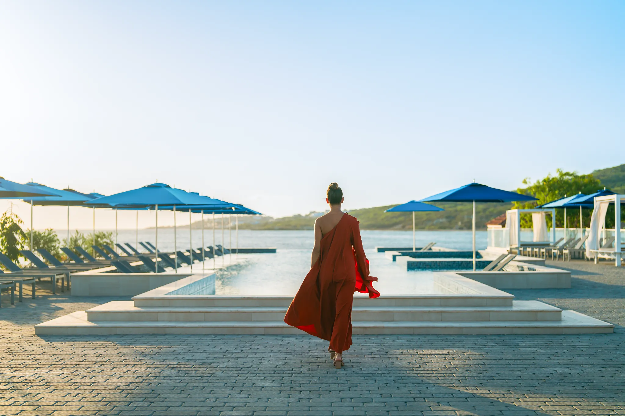 Woman walking toward infinity pool with ocean views at Dreams Curaçao Resort.